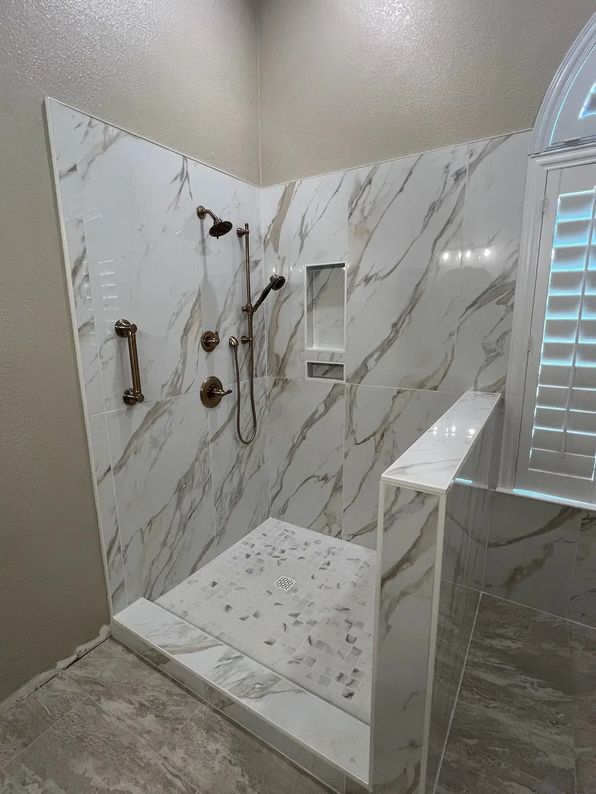 Walk-in shower finished in white marble subway tile with a built-in bench and niche