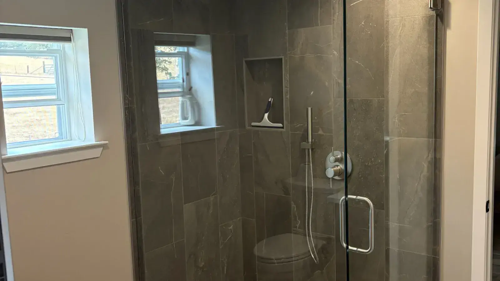 After: Bathroom after remodel with a gray-tile walk-in shower and frameless glass enclosure