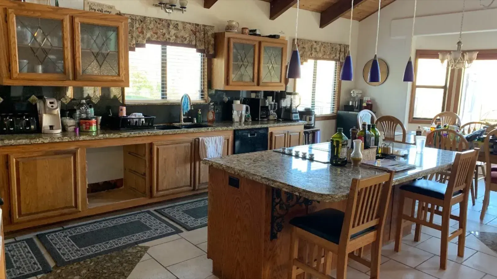 Before: Kitchen with oak cabinets and tile floors under a wood-beam ceiling before remodel