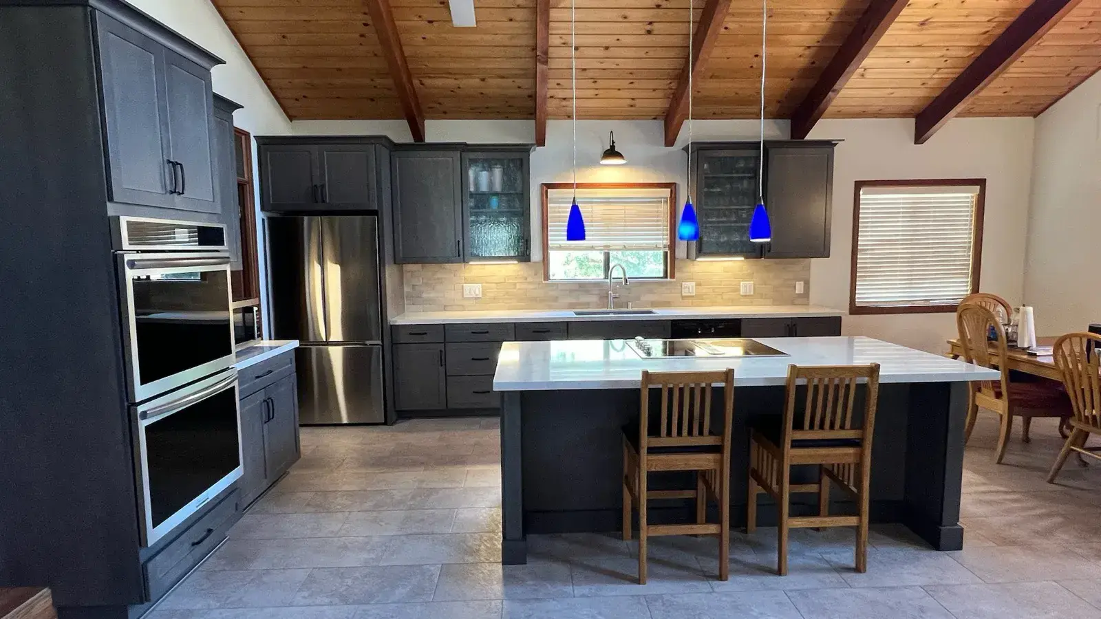 After: Remodeled kitchen with gray cabinets and a waterfall island under the same wood-beam ceiling