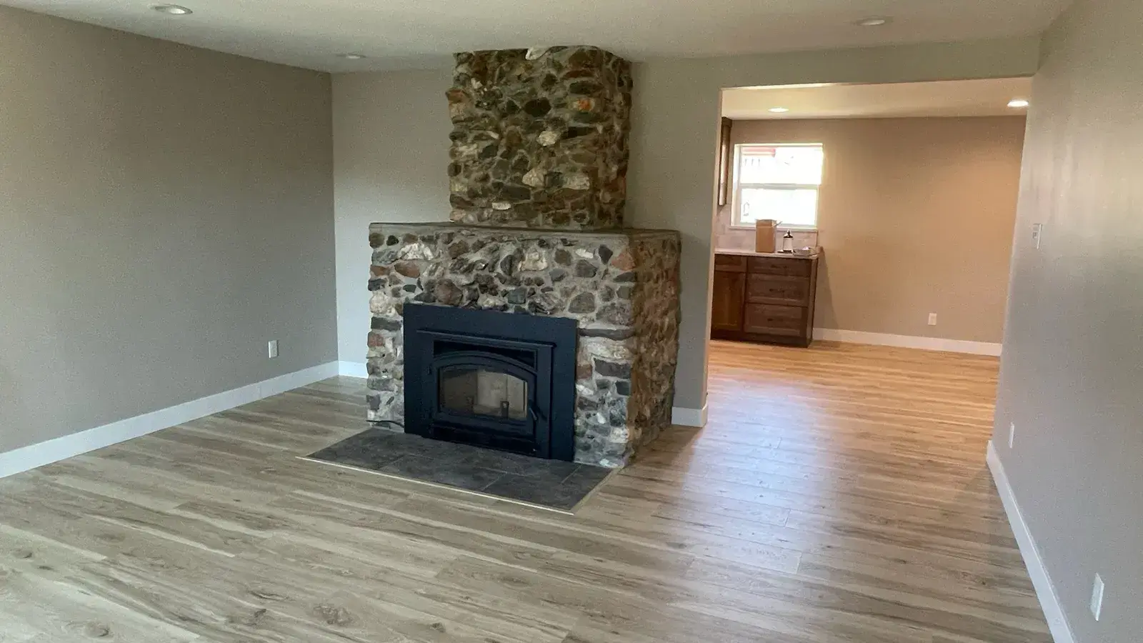 After: Living room rebuilt with new wood-look floors and a river-rock fireplace