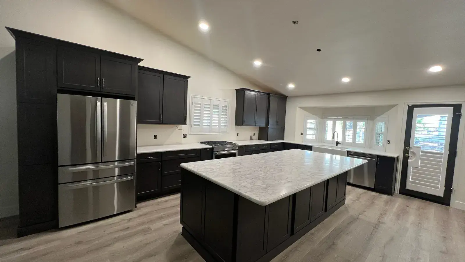 After: Open kitchen after remodel with dark cabinets and a white quartz waterfall island