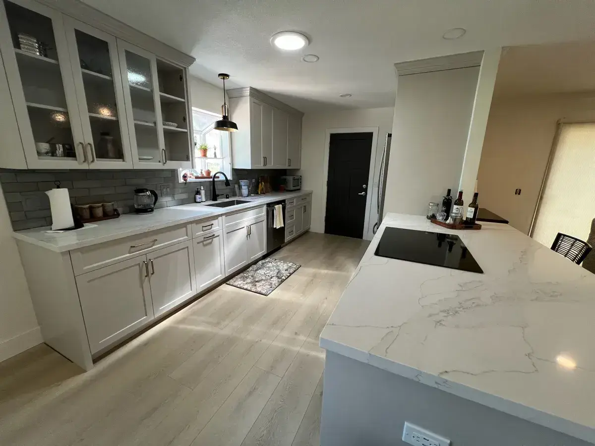 Finished modern white kitchen with a quartz waterfall island and gray subway backsplash