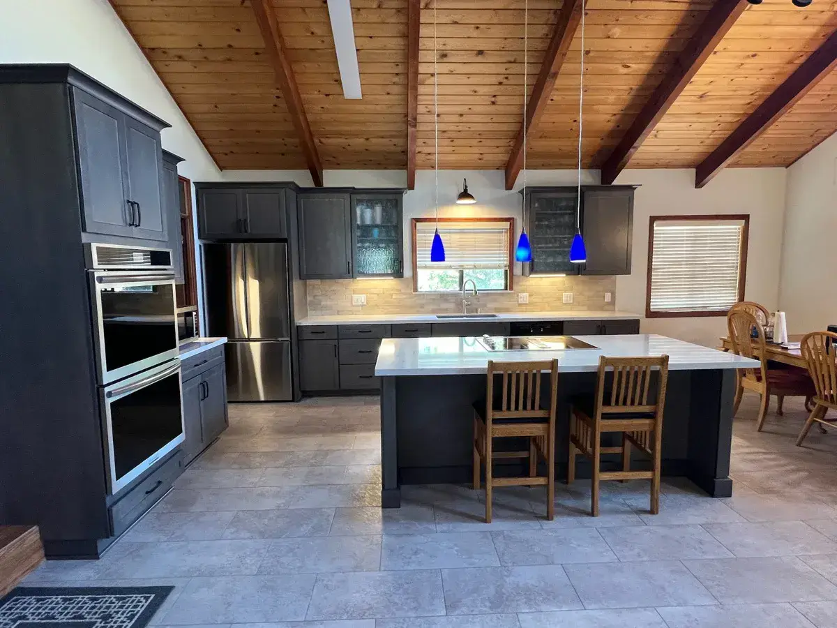 Finished kitchen with gray cabinets and a waterfall island under a wood-beam ceiling
